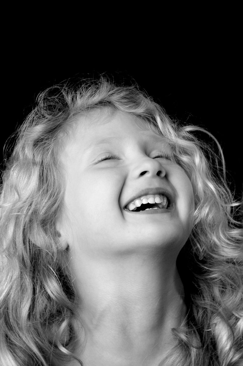 A young girl laughing with her head thrown back, in black and white