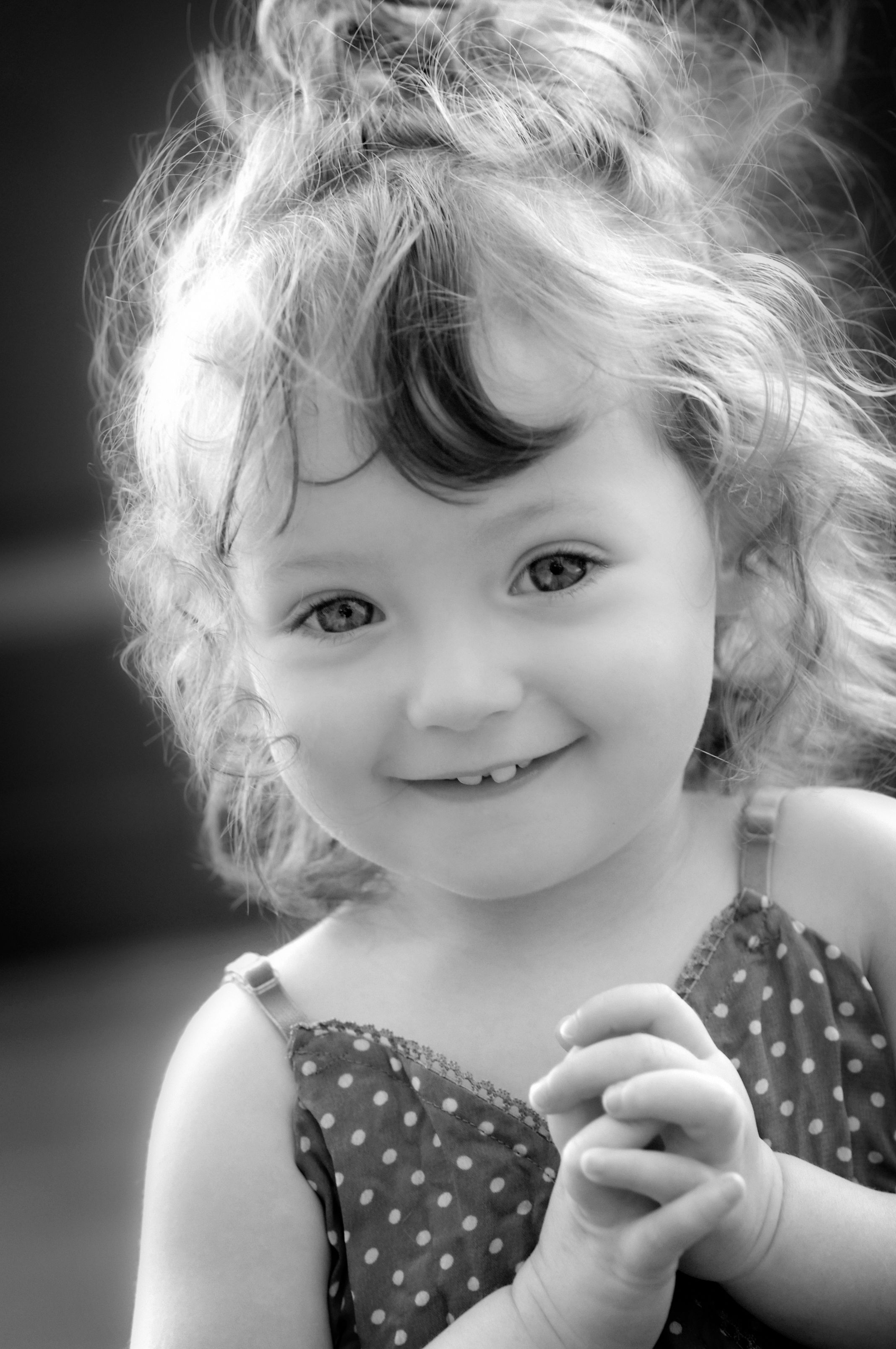 A curly haired toddler smiling straight at the camera, in black and white