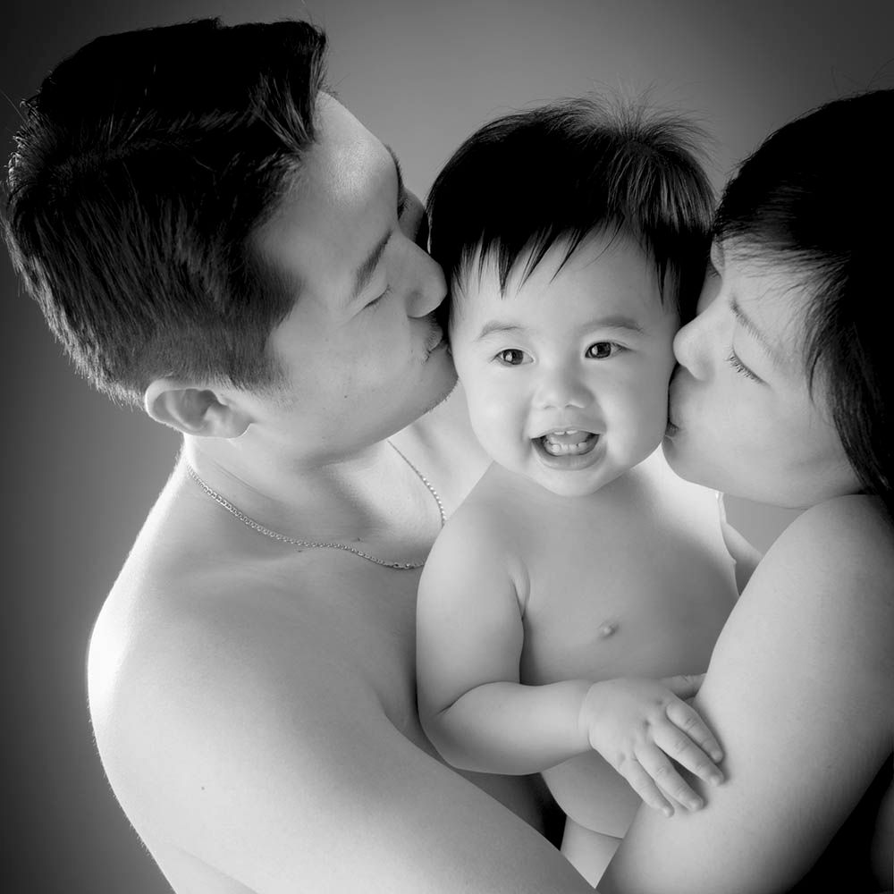A baby laughing while both parents kiss his cheeks