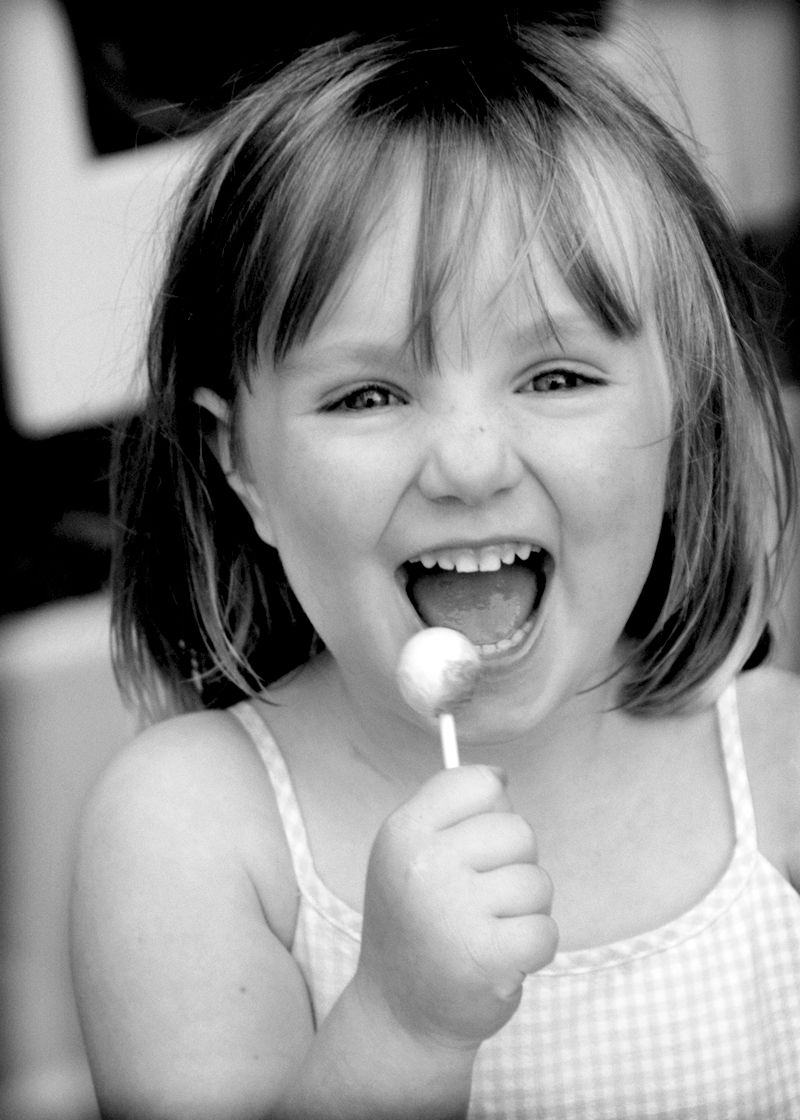 A girl grinning with a lollipop, in black and white