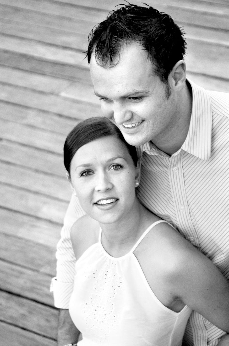 A couple leaning together against a weathered timber wall, in black and white