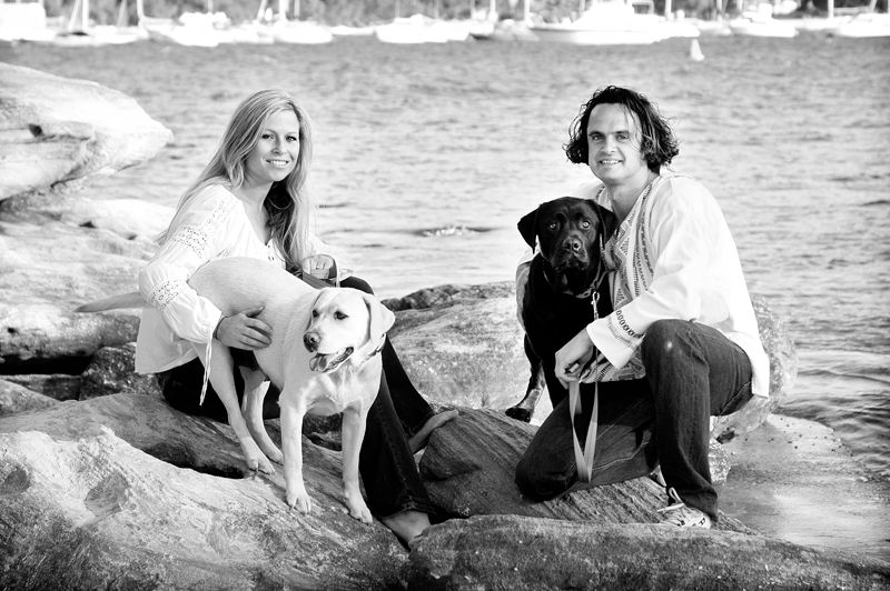 A couple sitting on the rocks by the water with their two dogs