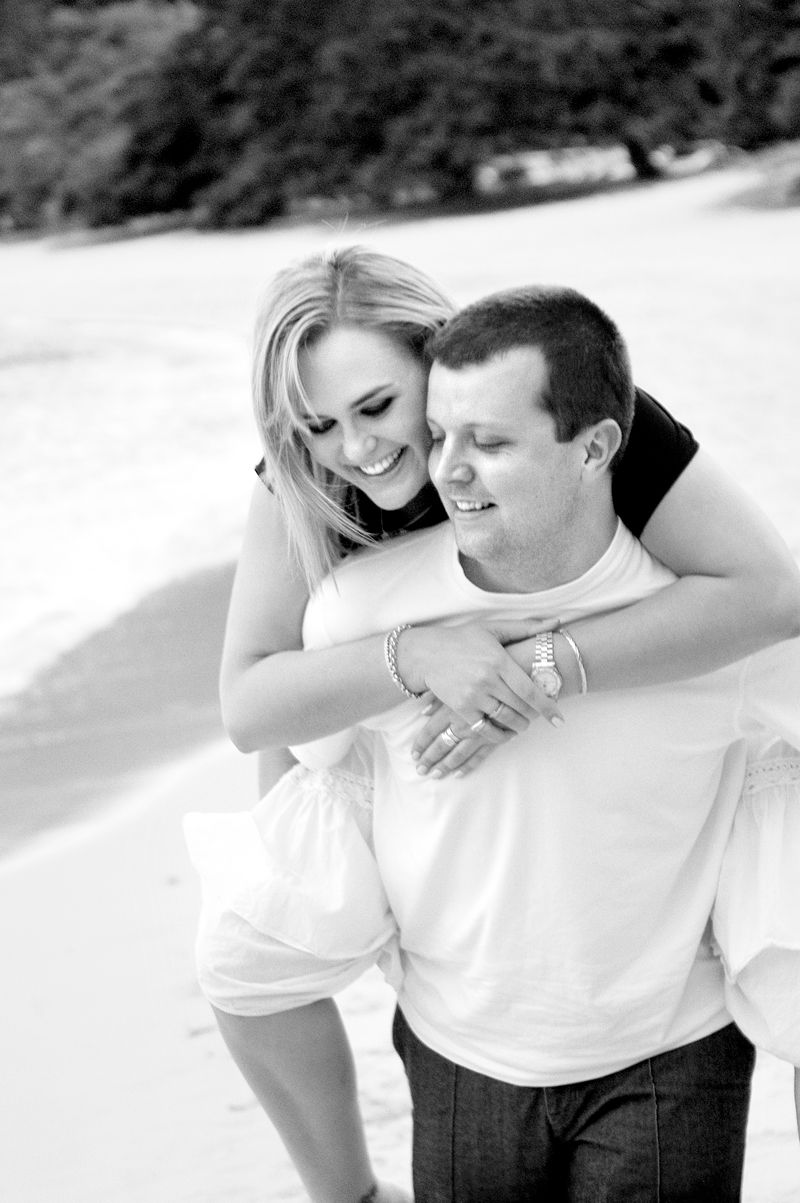 A man hugging his partner from behind, both laughing, in black and white