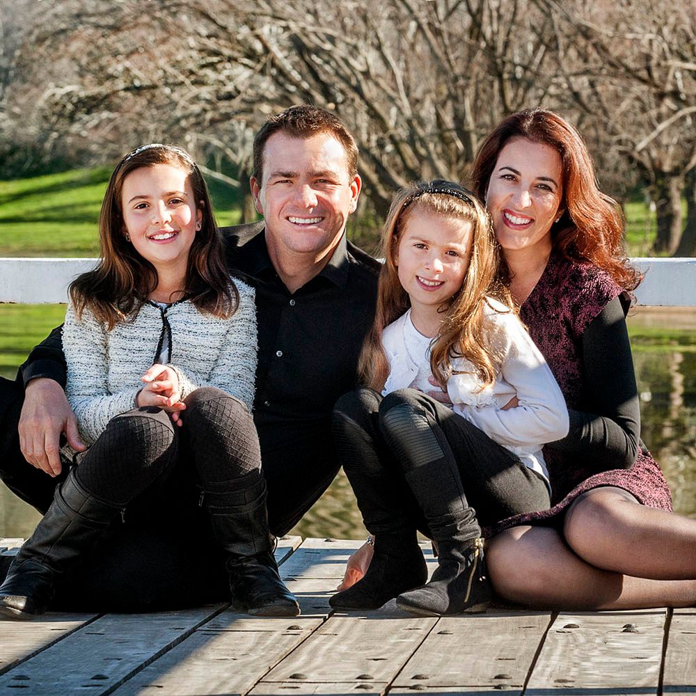 A family of four sitting close together on a park bench in autumn light