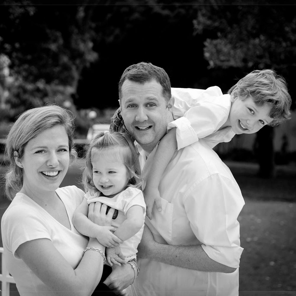 A young family of four holding each other and laughing, in black and white