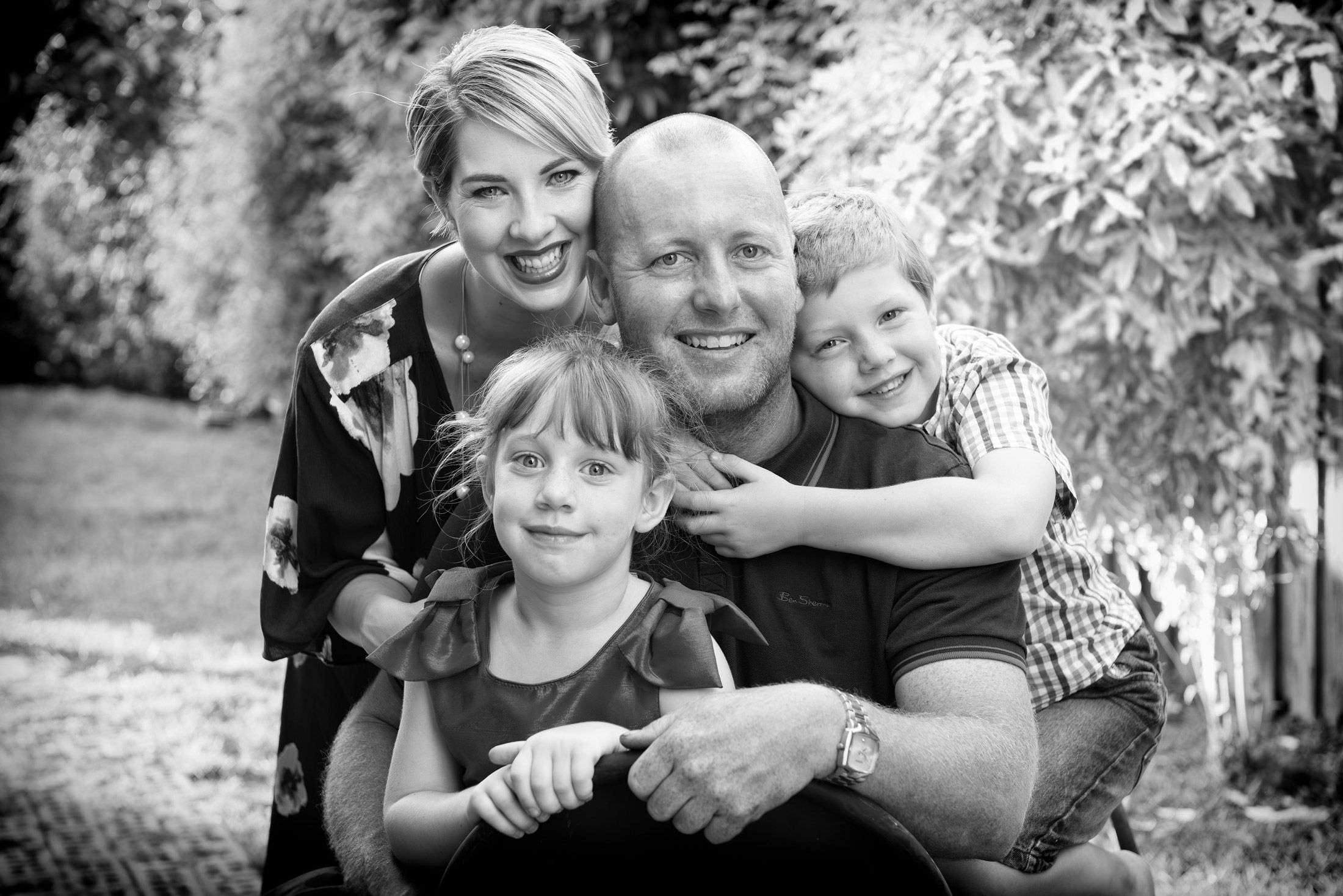 A family of four in a laughing huddle, in black and white