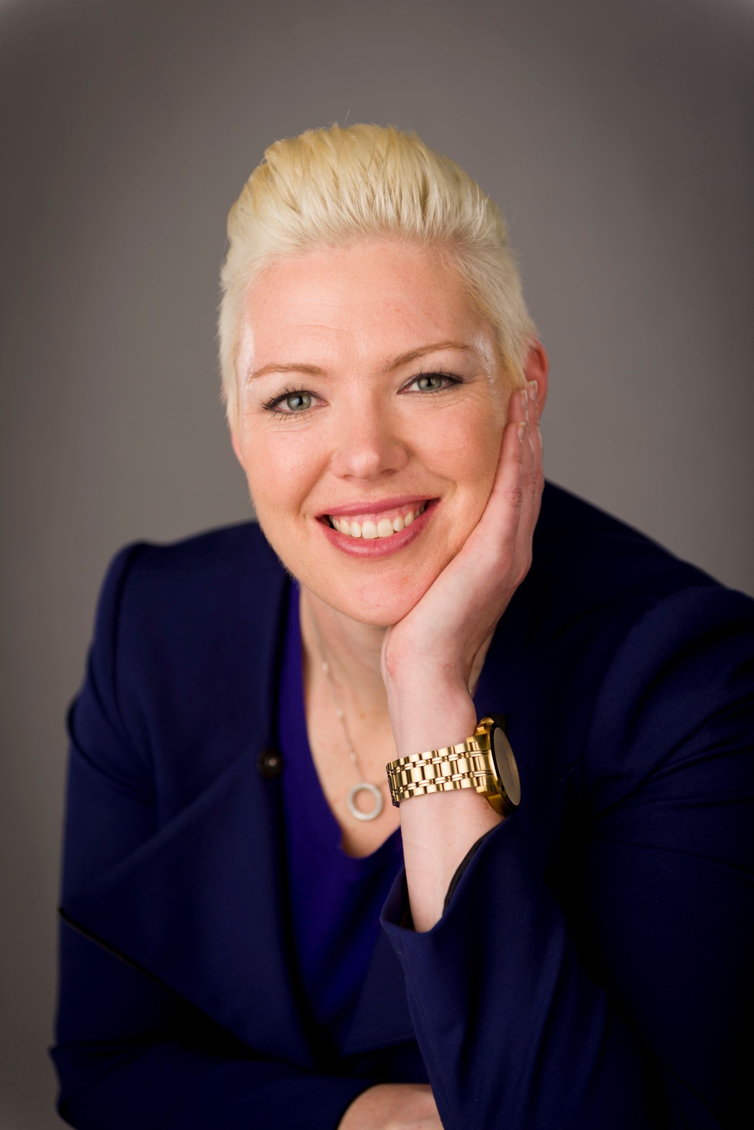 A woman in a navy jacket smiling with her chin on her hand