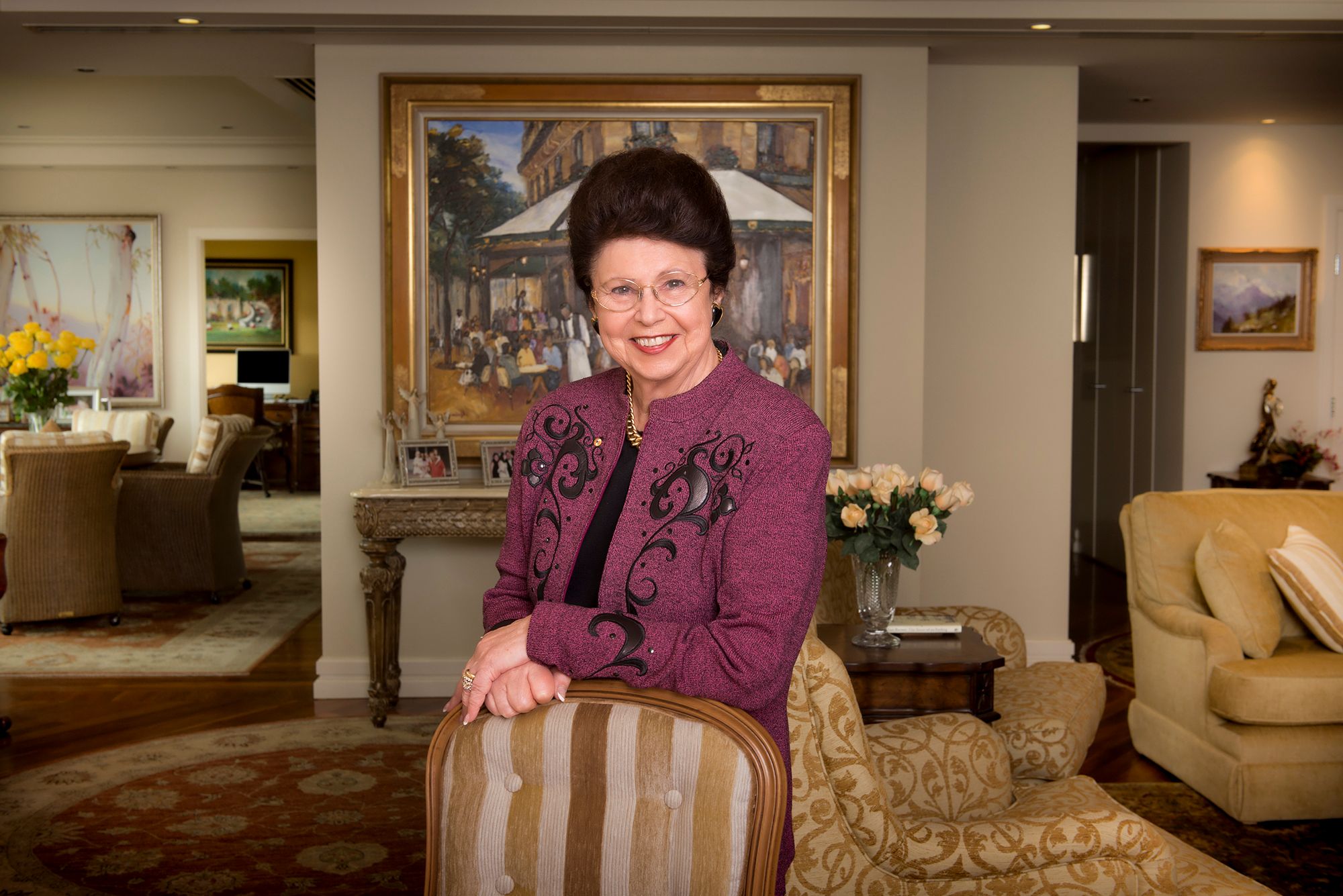 An older woman seated in her living room among her paintings