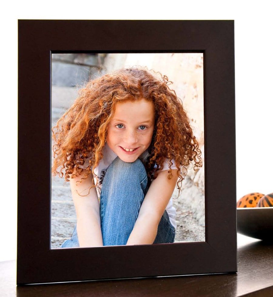 A framed portrait of a smiling girl with red curls, standing on a sideboard